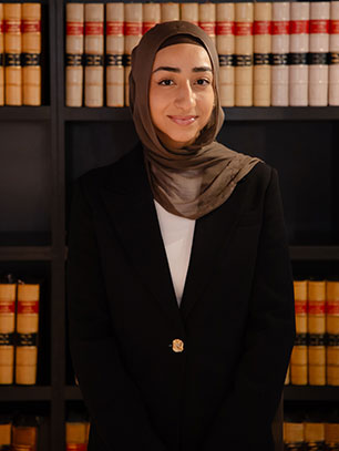 Professional portrait of a Krayemandco criminal lawyer wearing a black blazer and brown hijab standing in front of a law library at a Criminal defence firm Sydney CBD.