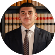 Circular portrait of a Krayemandco criminal lawyer wearing a navy suit and geometric tie, with a legal library in the background in our Criminal defence firm Sydney CBD office.