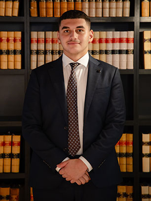 Professional portrait of a Krayemandco criminal lawyer in a navy suit and geometric tie with hands folded, standing in front of a law library at our Criminal defence firm Sydney CBD.