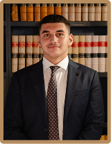 Professional portrait of a Krayemandco criminal lawyer, wearing a navy blue suit and geometric tie, standing in front of a law library bookshelf in our Criminal defence firm Sydney CBD office.