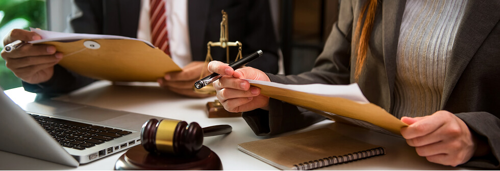 Two Sydney criminal defence lawyers in business attire collaborate at a desk with a laptop, gavel, and legal scales, holding folders.