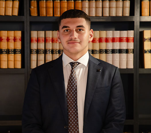 Professional portrait of a Krayemandco criminal lawyer in a navy suit and geometric tie standing in front of a law library at a Criminal defence firm Sydney CBD.