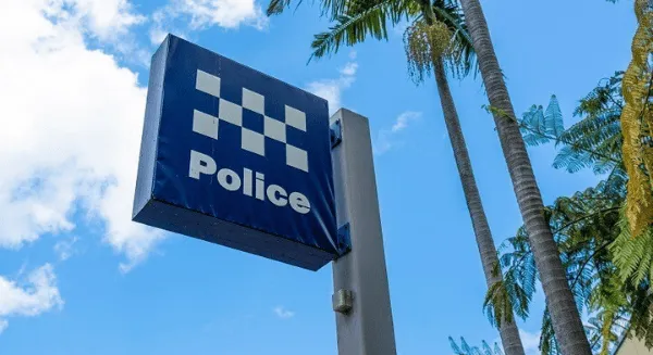 A blue and white checkered NSW Police station sign on a post against a bright blue sky with palm trees, representing the first point of contact for a Criminal defence lawyer Sydney firm.